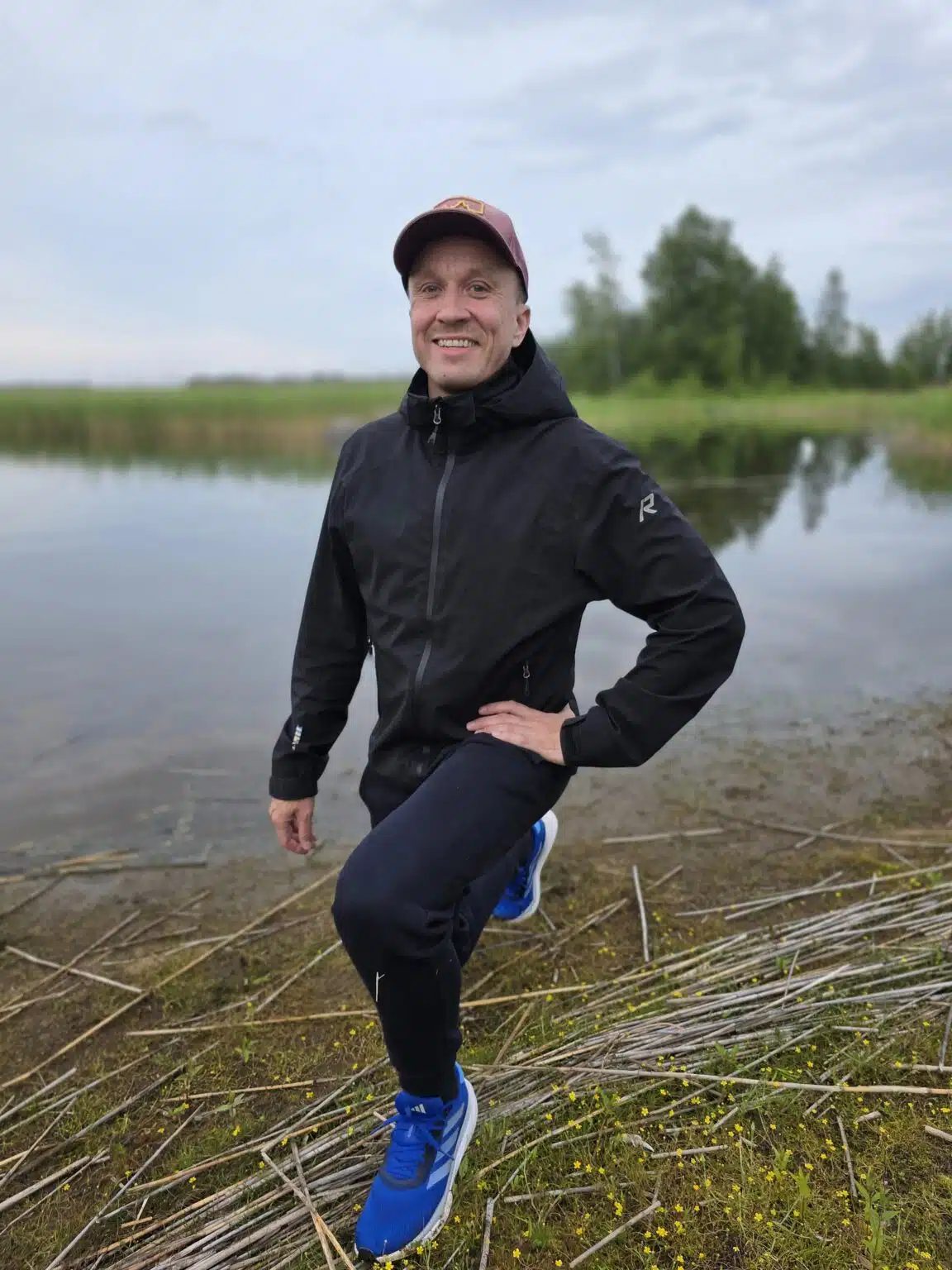 Antti Ruskeala liikkumassa järven rannalla kaislikossa, urheiluvaatteissa ja lippalakissa.