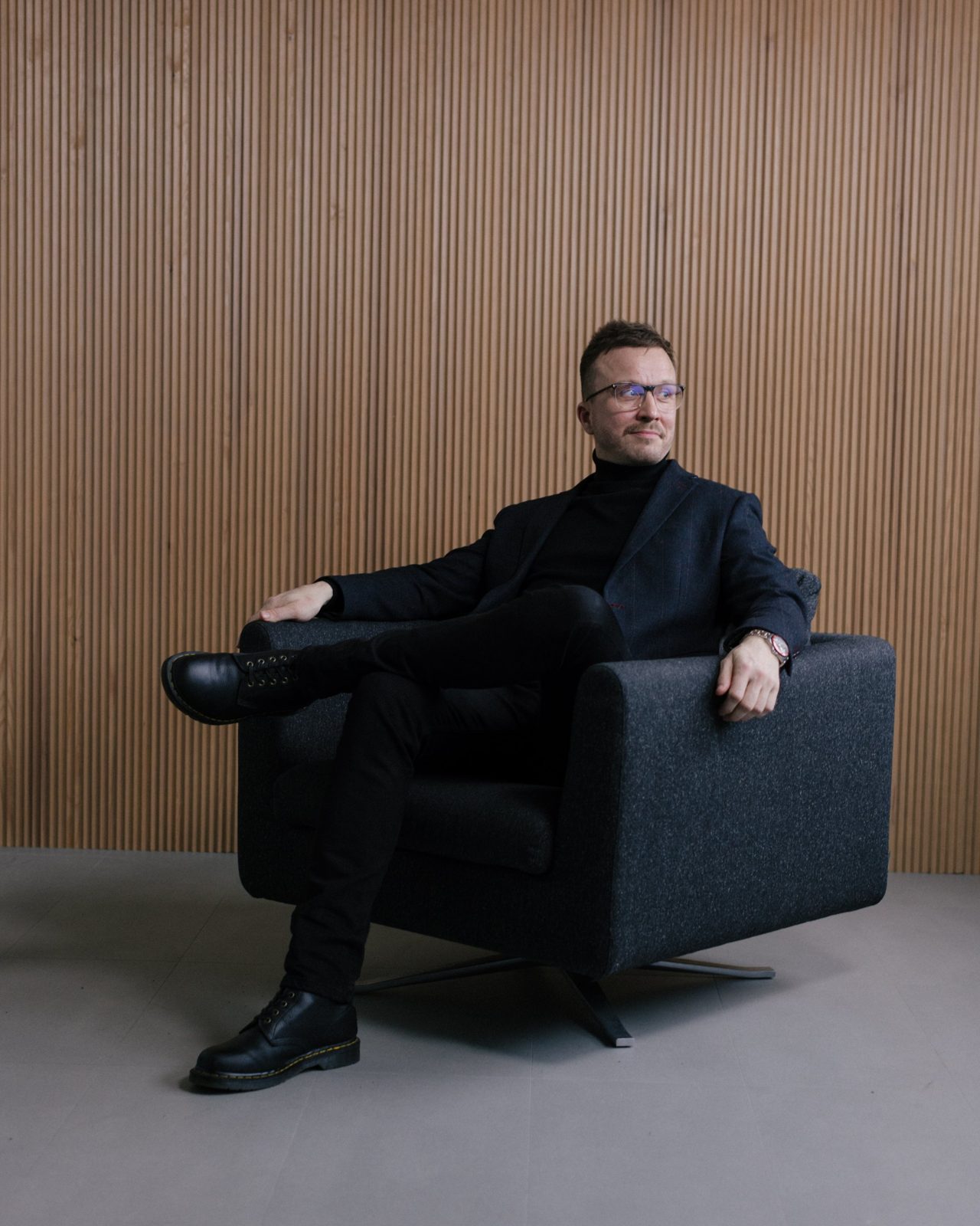 Antti Ruskeala istuu nojatuolissa tummassa pikkutakissa ja poolopaidassa puupaneloidun seinän edessä.